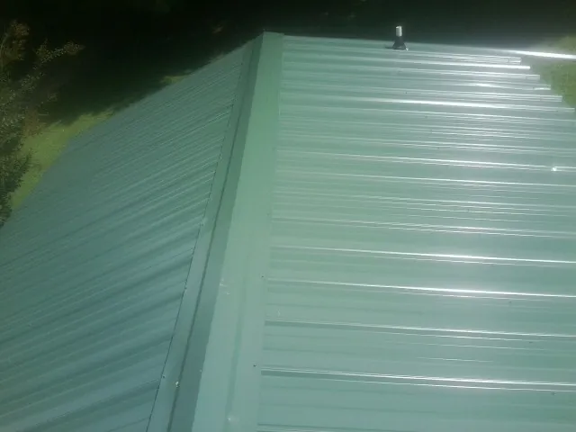 New green metal panels meeting at the ridge of a roof — Flat Roof Repair work by our crew in Providence